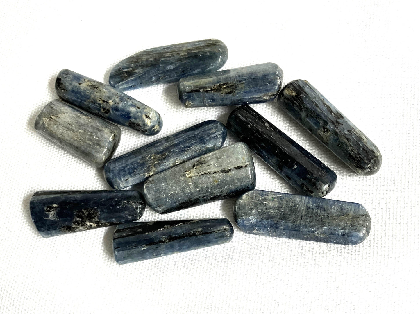 Blue Kyanite Crystals showing the different patterns and colors on a white fabric background