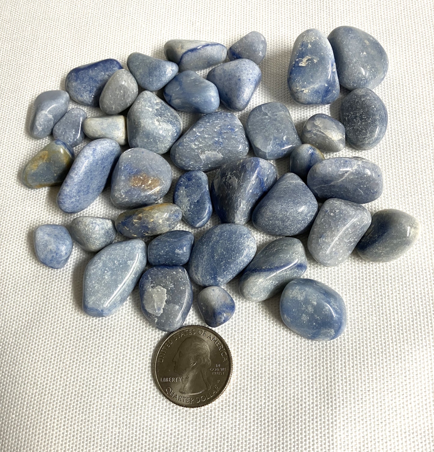 Back view of Blue Quartz Crystals on a white fabric background with a quarter for scale