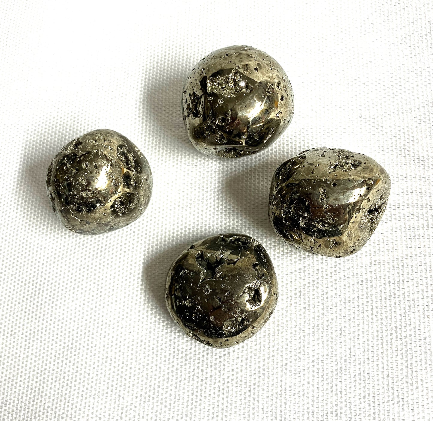 A group of Tumbled Pyrite Crystal AKA Fool's Gold showing different views on a white fabric background