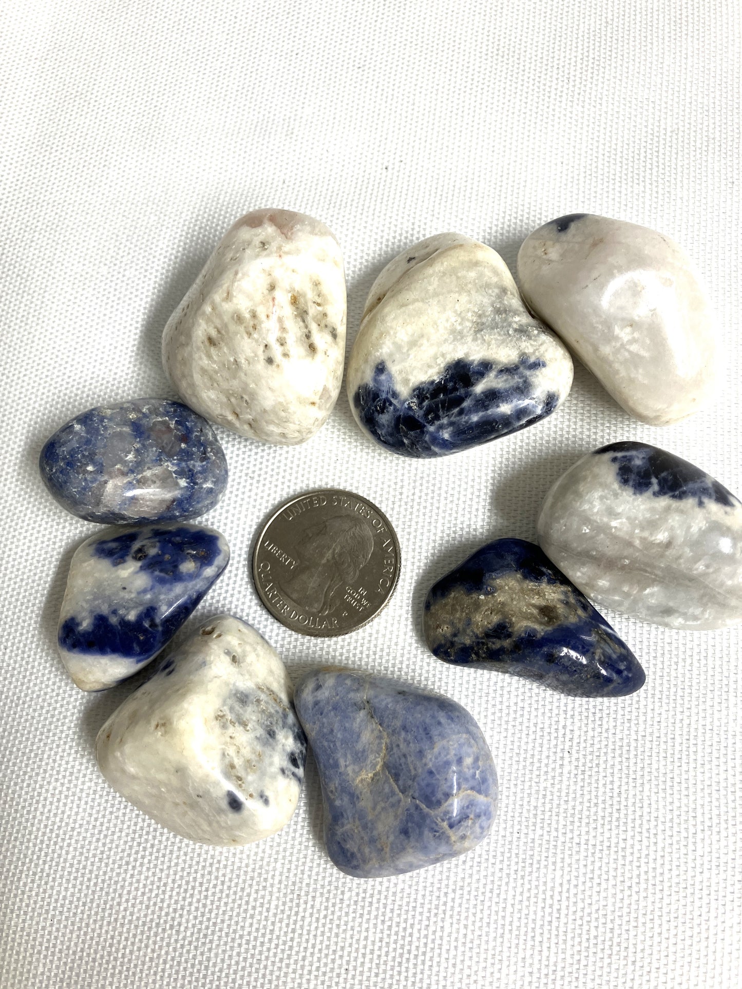 Tumbled sodalite stones with a quarter for size comparison on a white background