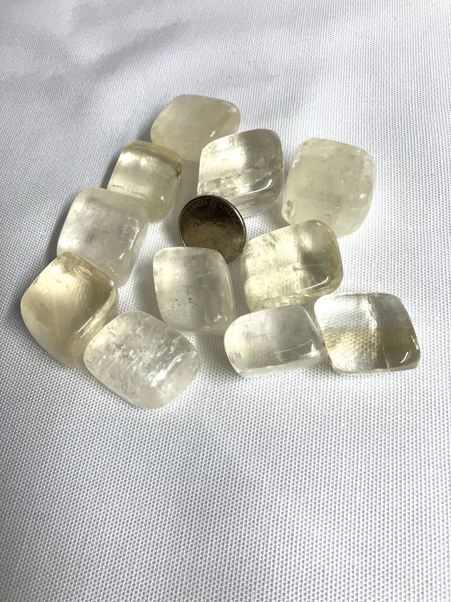 Yellow Calcite Tumbled Crystals shown with a quarter for scale on a white background