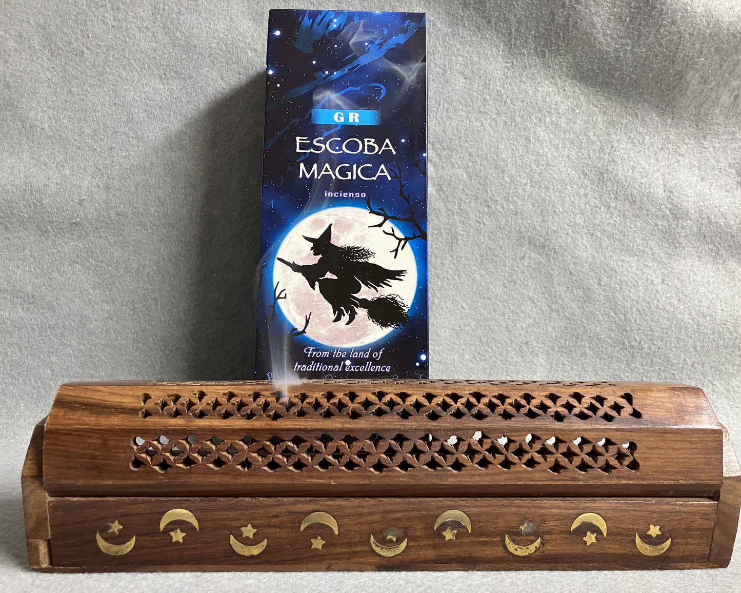 GR Magic Broom incense shown with the Spanish title, Escoba Magica showing. Displayed with a decorative wooden incense burner on a gray background