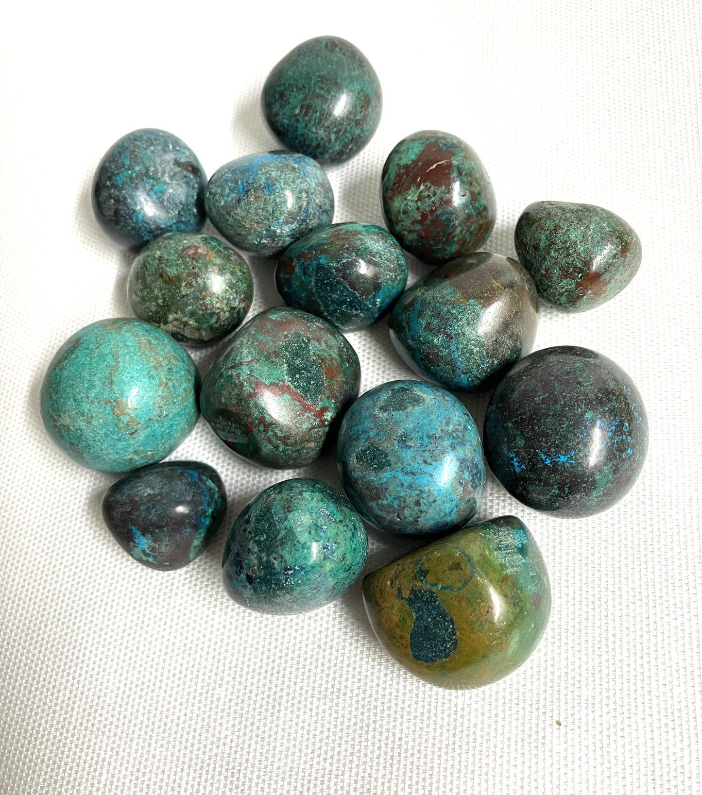 Back side of Chrysocolla Crystals showing the patterns and colors displayed on a white fabric backgroundl
