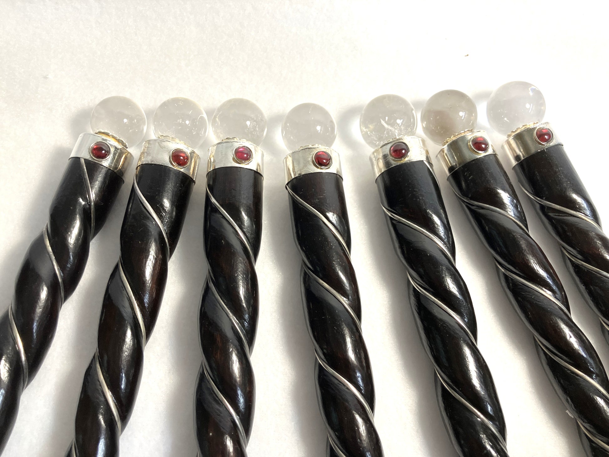 Closeup of a group of rosewood twisted wands showing the quartz orb, red accent and silver accents shown on a white background