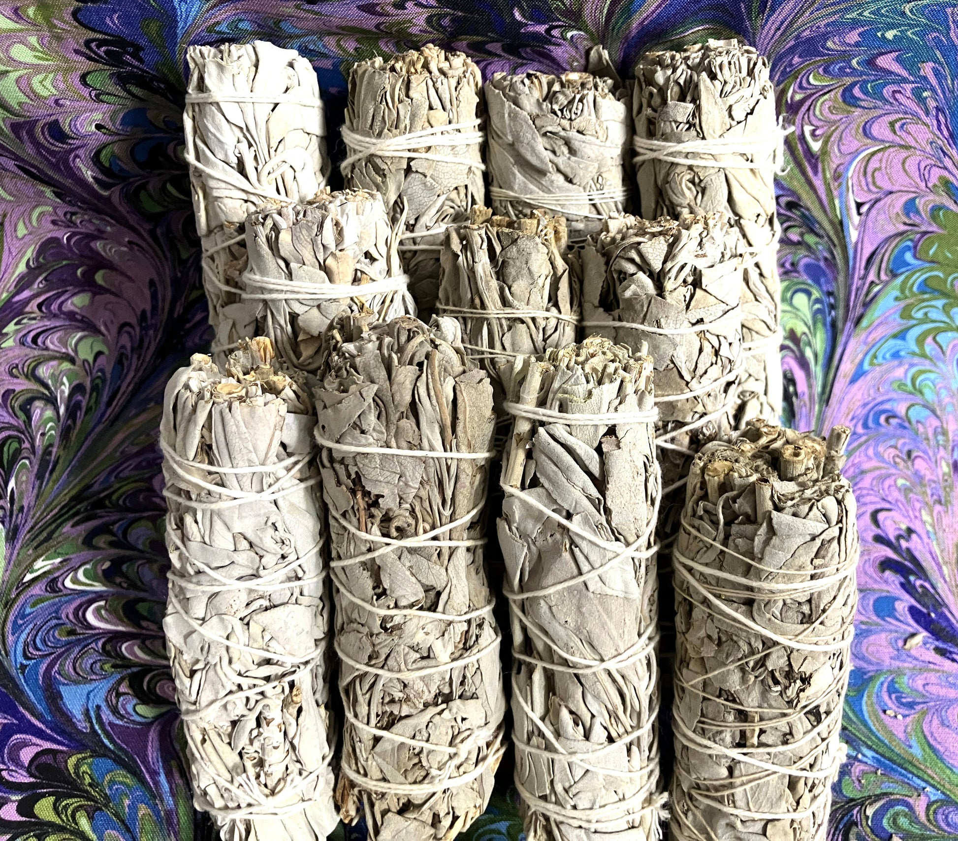 Group of eleven White Sage smudge sticks showing the ends on a purple and green swirled background
