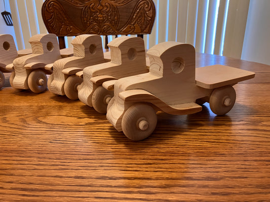 Wooden toy pickups on a wooden table with a decorative chair in the background.