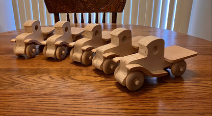Set of wooden toy trucks on a wooden table with a chair in the background.