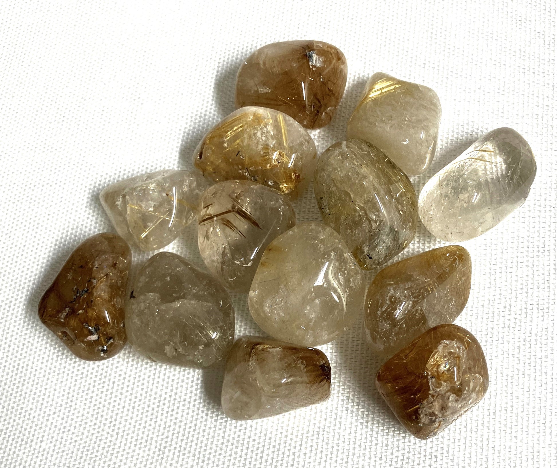 Closeup of a group of tumbled Rutilated Quartz gemstones on a white fabric background