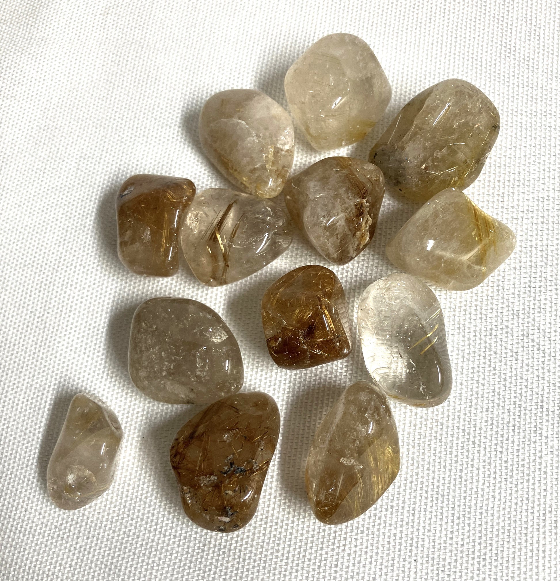 Collection of tumbled Rutilated Quartz gemstones on a white fabric background