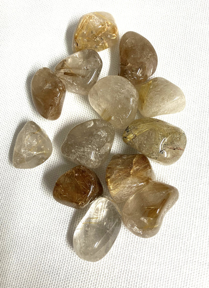 Collection of Rutilated Quartz gemstones on a white fabric background showing another side