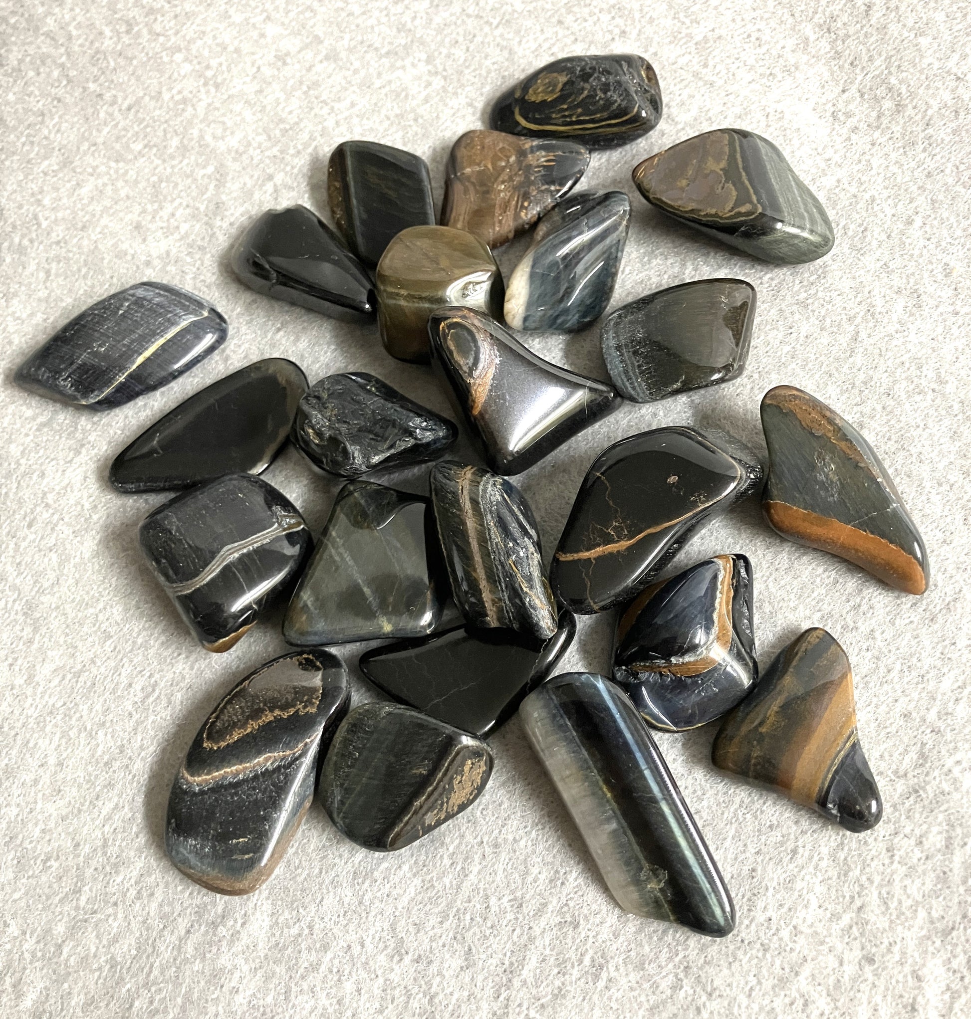 Tumbled Blue Tiger Eye Crystal AKA Hawks Eye AKA Falcons Eye on a light gray background