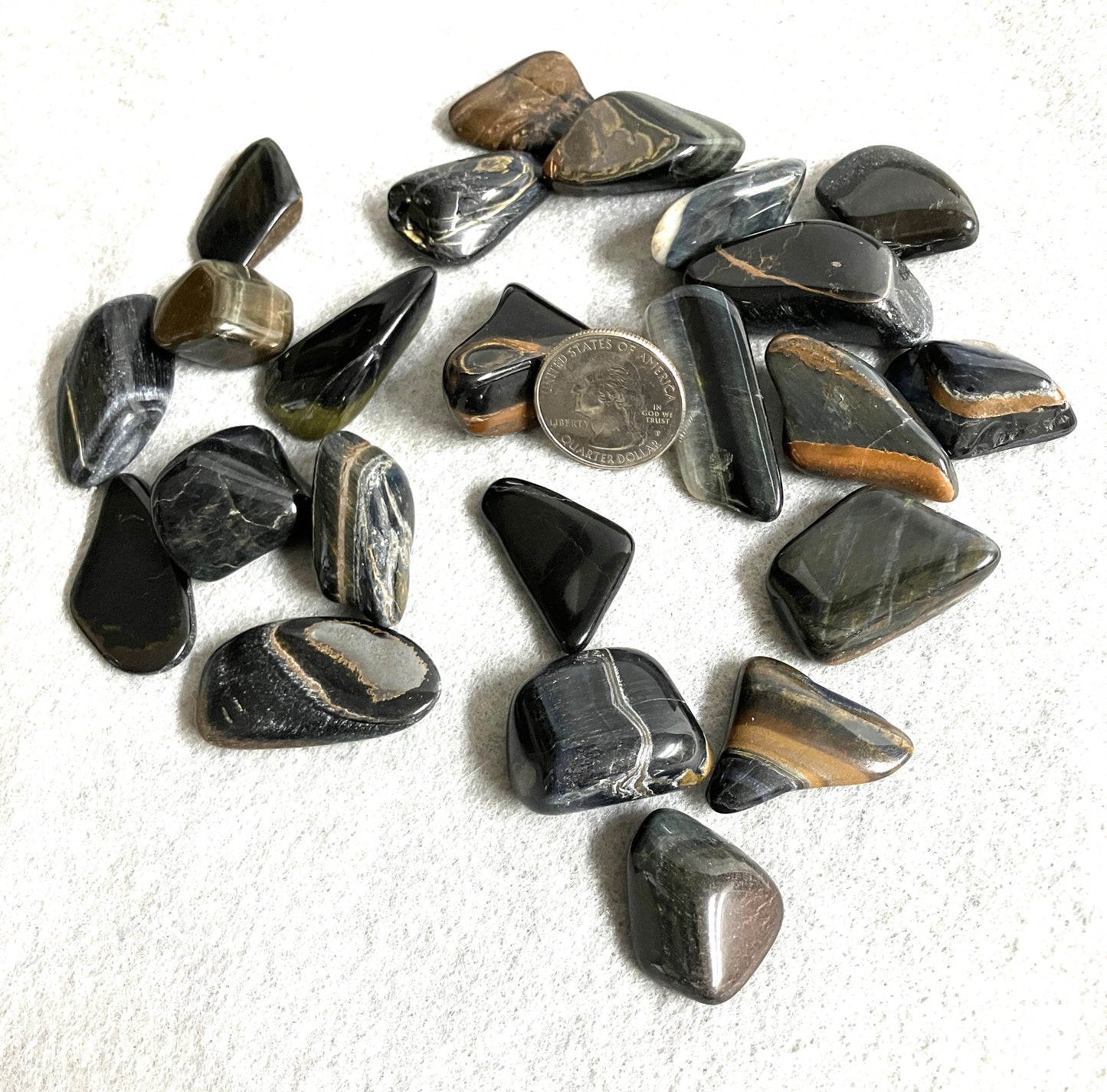 Front view of Blue Tiger Eye Crystal AKA Hawks Eye AKA Falcons Eye on a white surface with a quarter for scale.