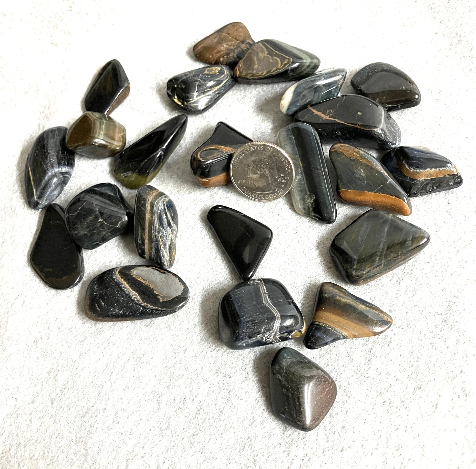 Front view of Blue Tiger Eye Crystal AKA Hawks Eye AKA Falcons Eye on a white surface with a quarter for scale.