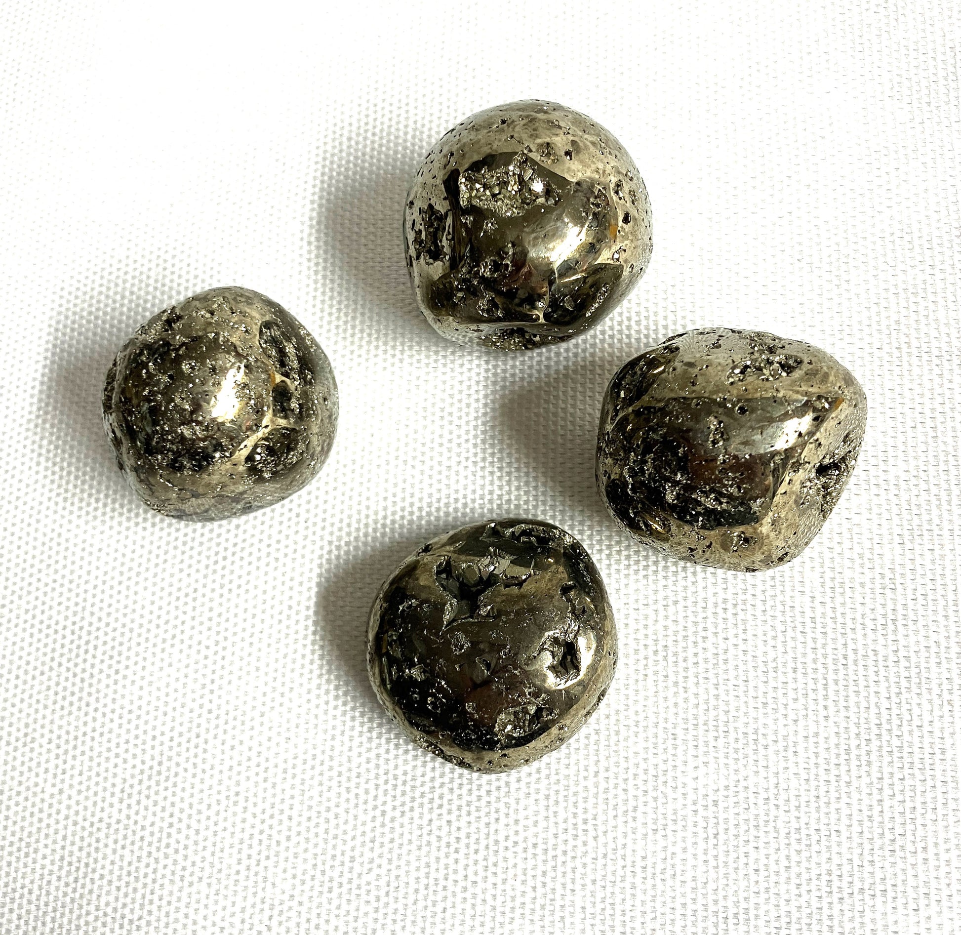 A group of Tumbled Pyrite Crystal AKA Fool's Gold showing different views  on a white fabric background
