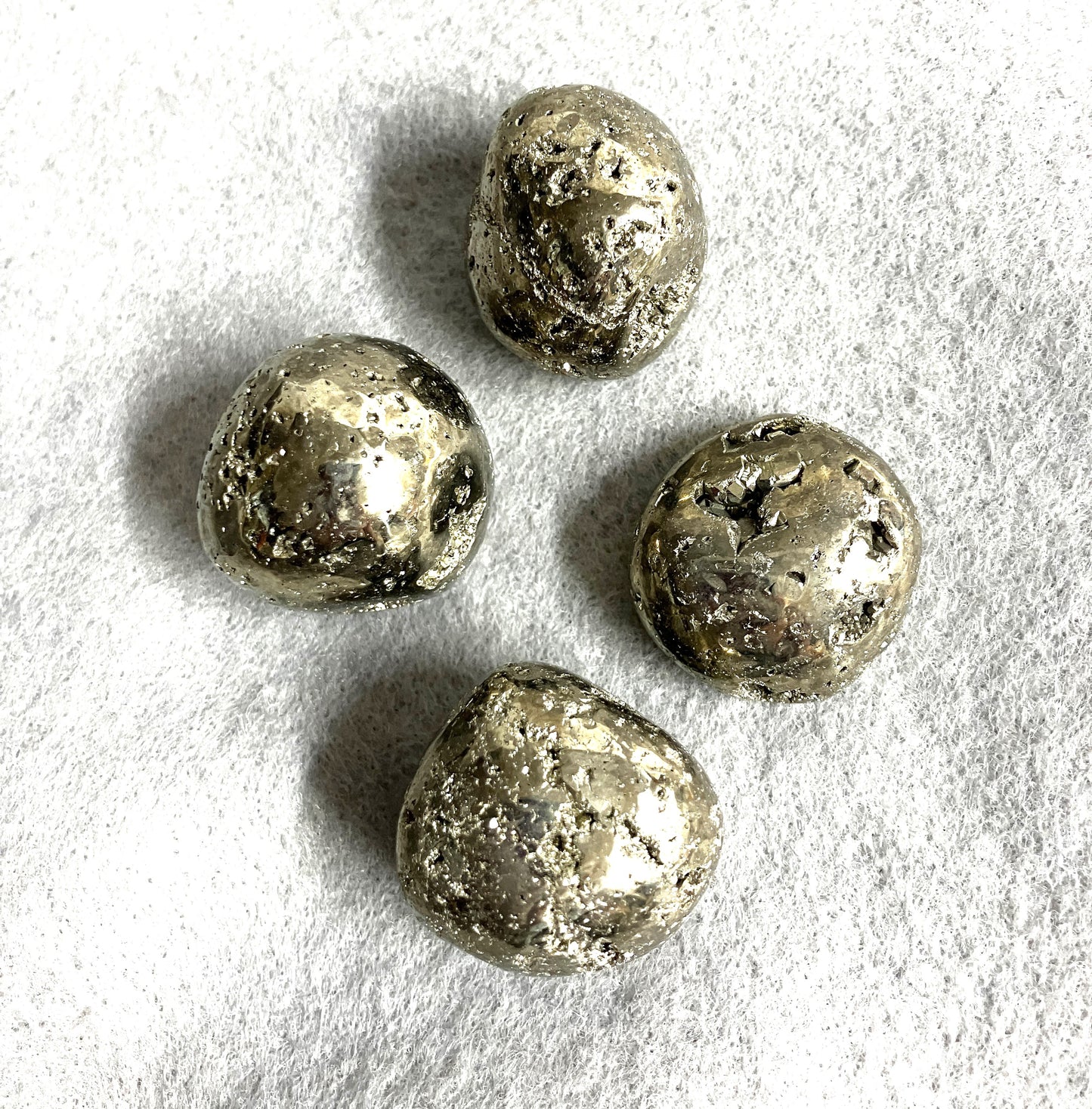 Tumbled Pyrite Crystal AKA Fool's Gold  shown on a textured white surface