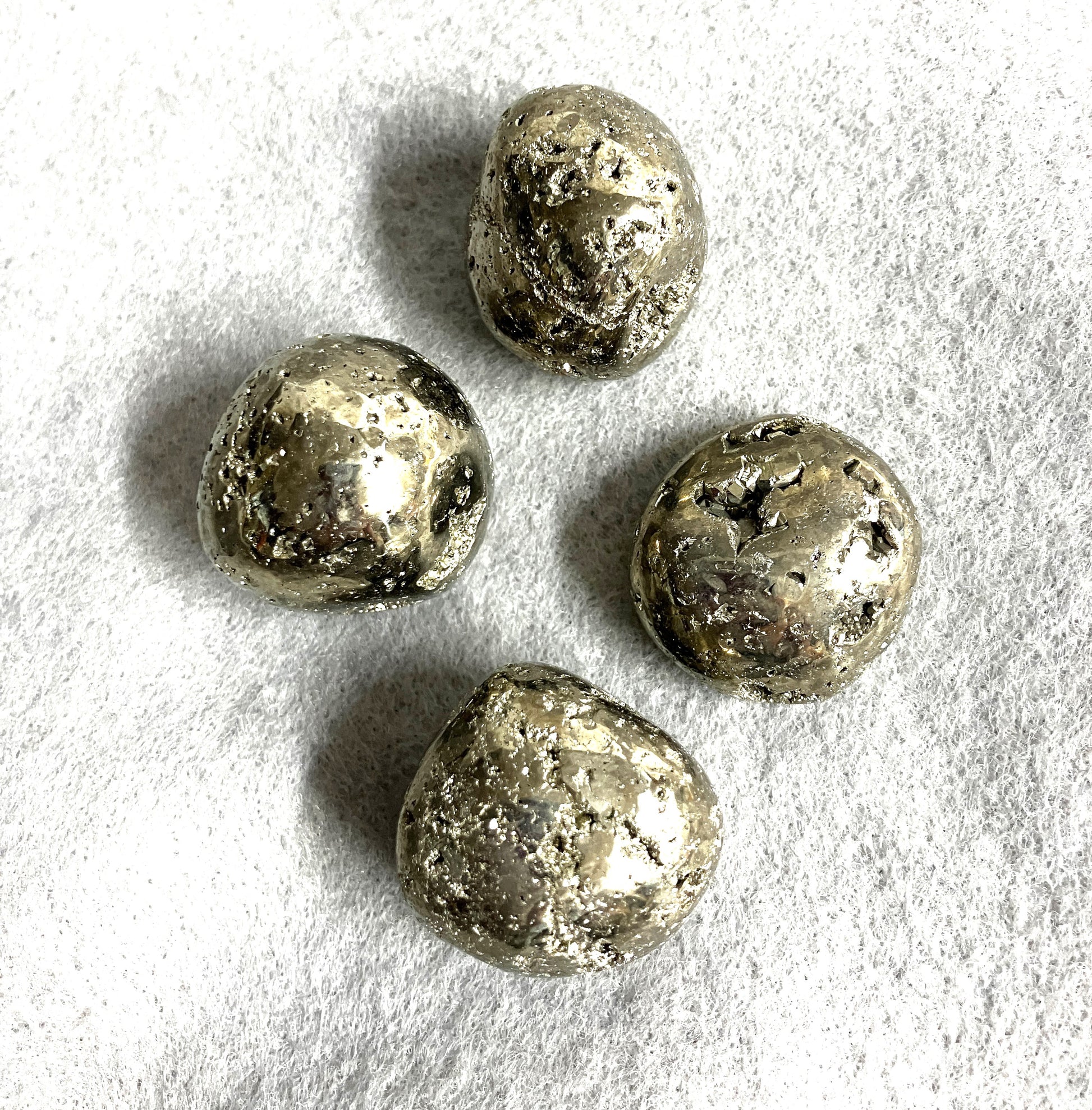 Tumbled Pyrite Crystal AKA Fool's Gold  shown on a textured white surface