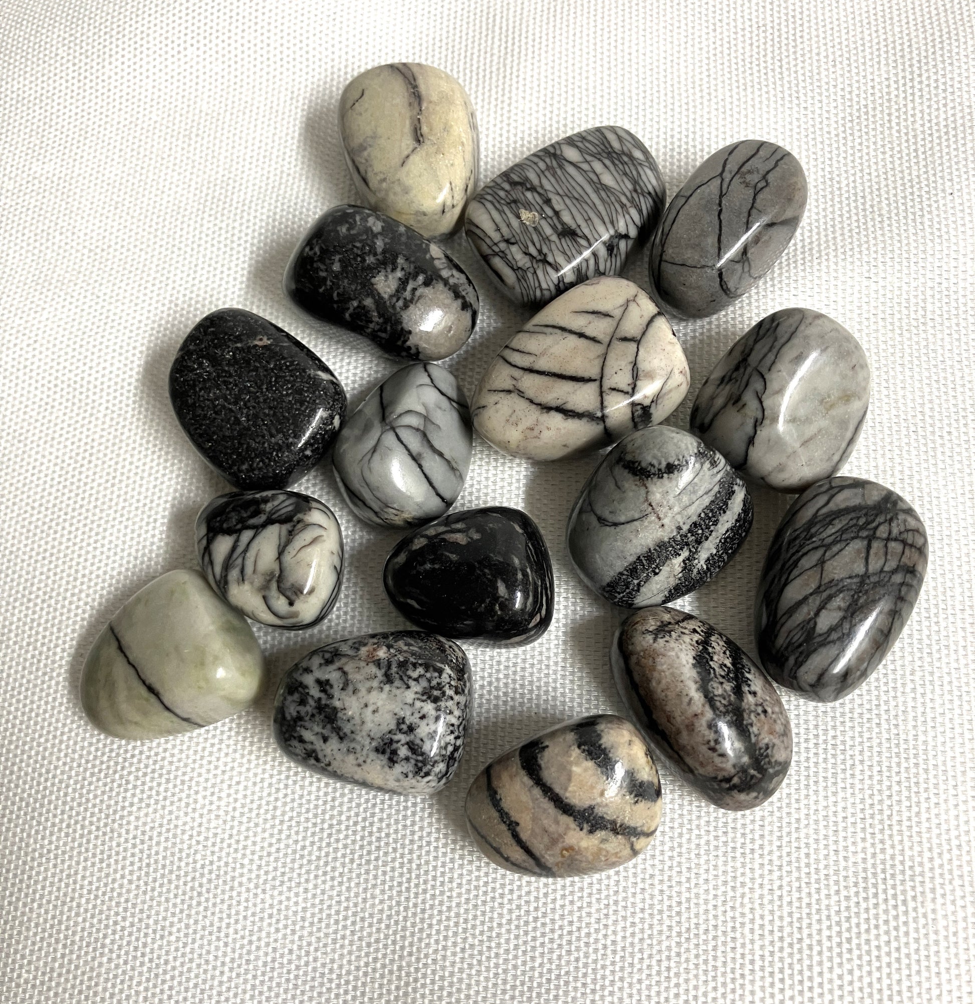 Tumbled Spider Web Jasper Crystals on a white fabric background