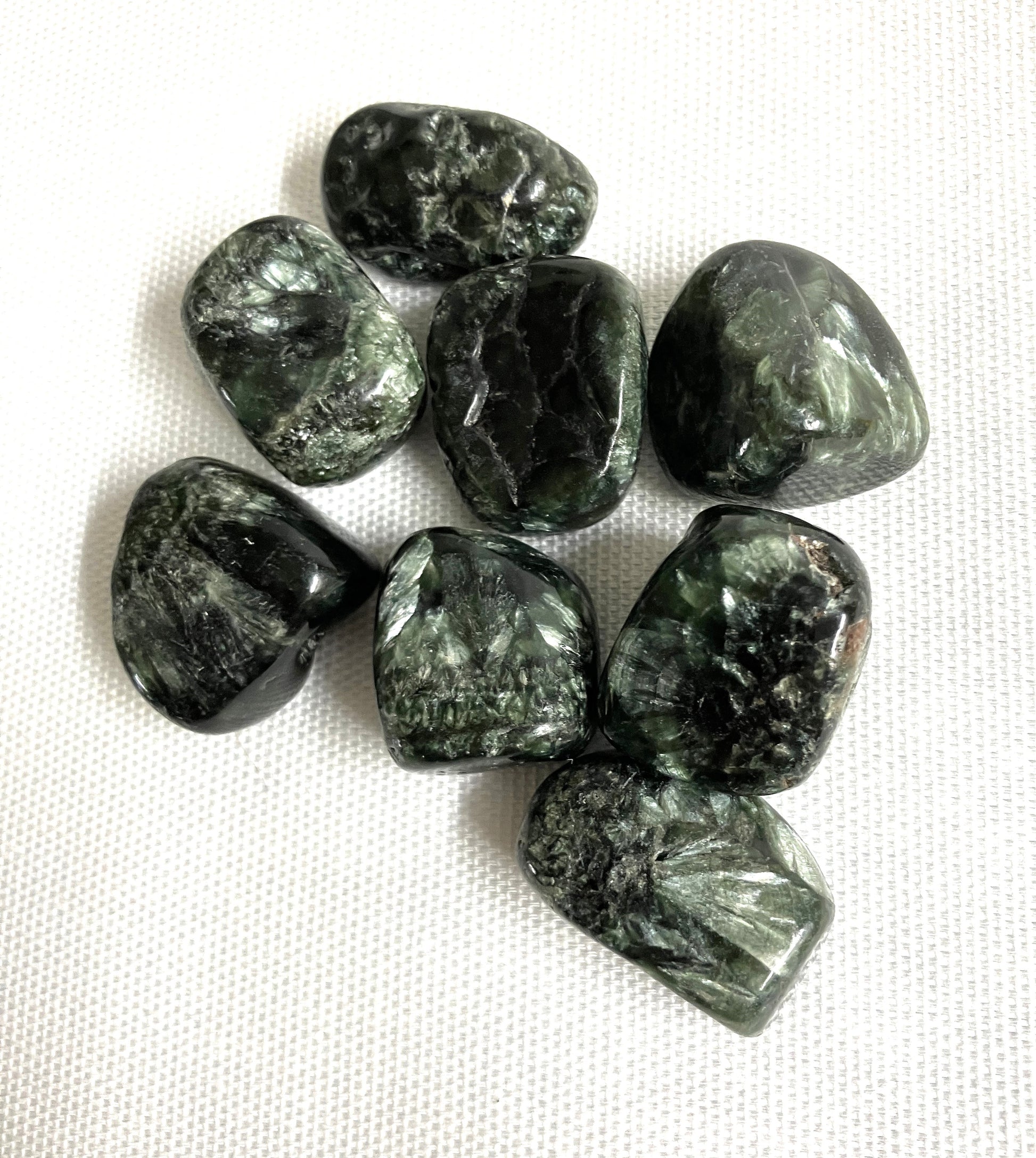 A view of Seraphinite Crystals showing the various patterns and colors on a white fabric background