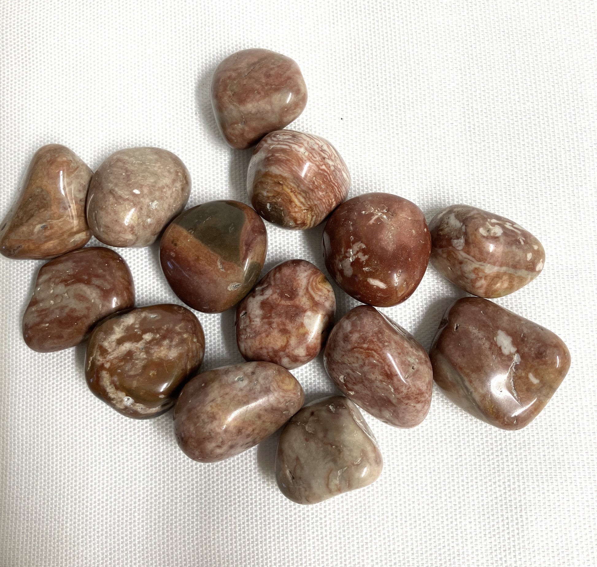 Collection of Tumbled Crazy Lace Agate Crystals on a white fabric background