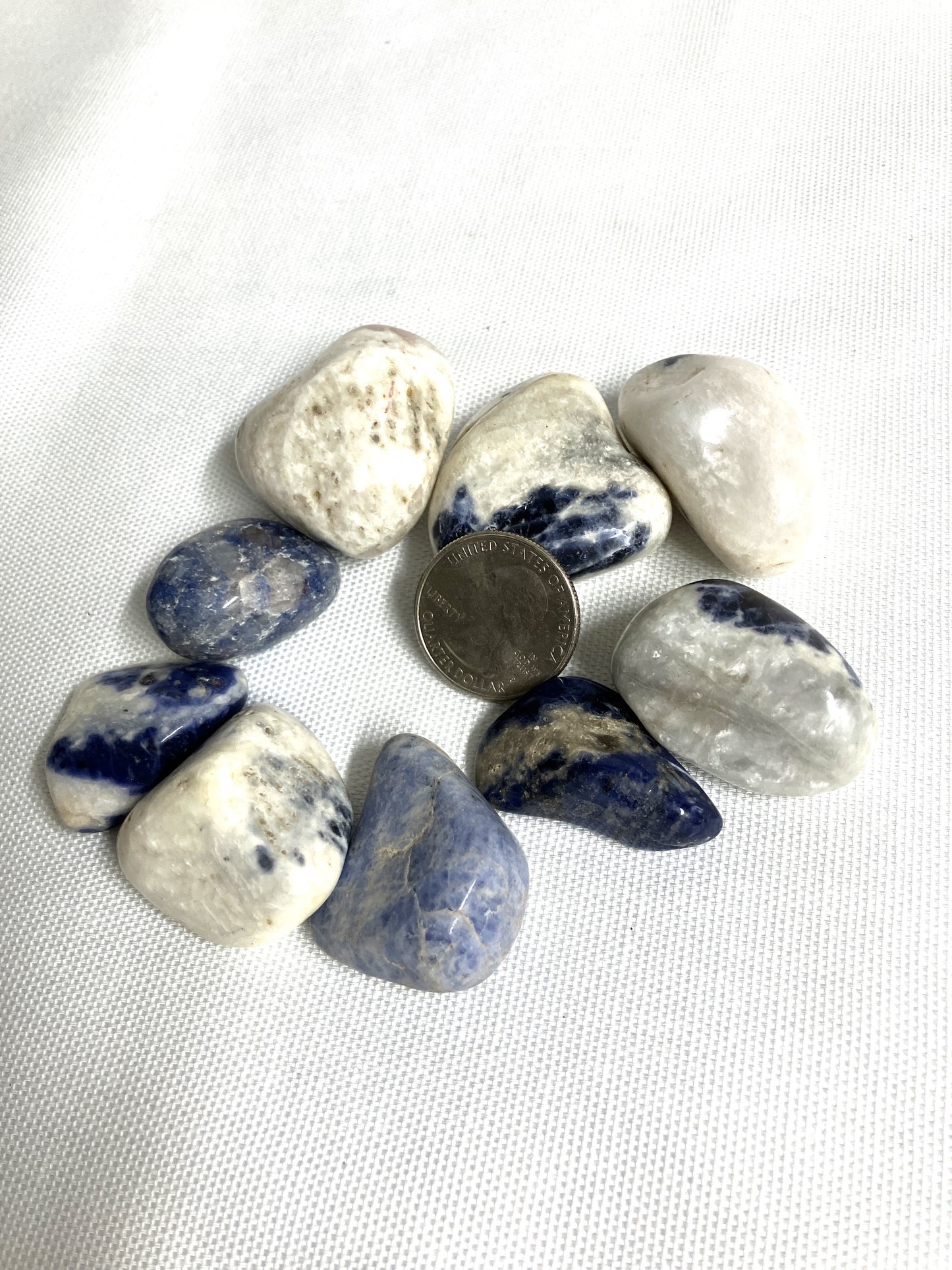 Tumbled Sodalite Crystals on a white background with a quarter for scale.