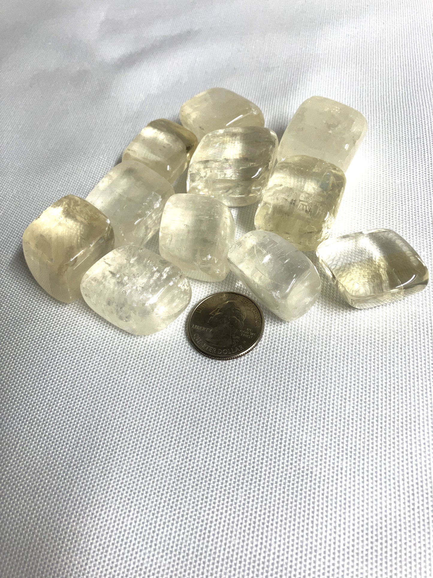 Yellow Calcite Tumbled Crystals shown with a coin for size on a white fabric background