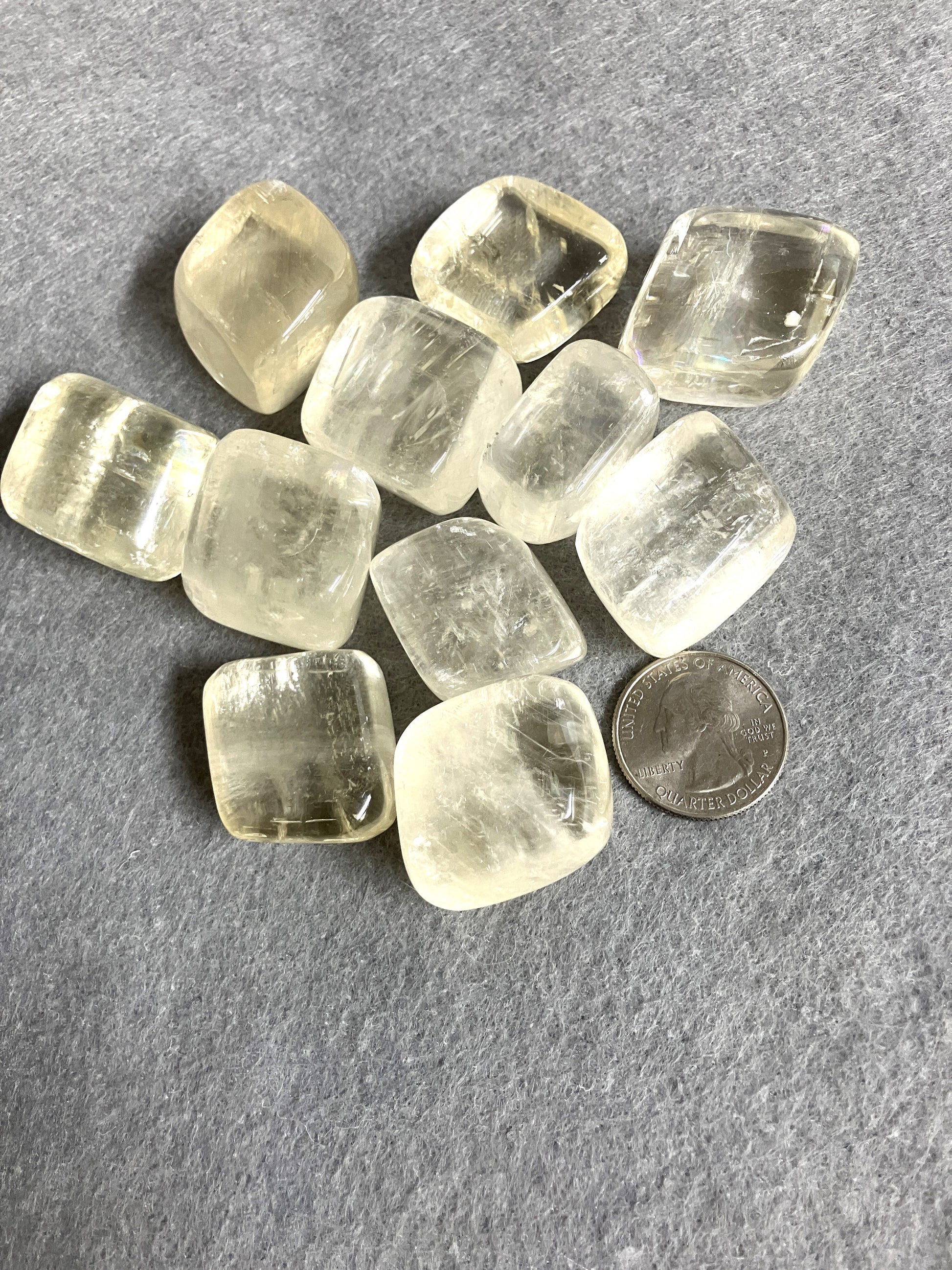 Group of Yellow Calcite Tumbled Crystals on a gray surface with a quarter for scale