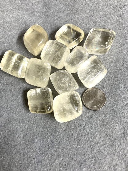 Group of Yellow Calcite Tumbled Crystals on a gray surface with a quarter for scale
