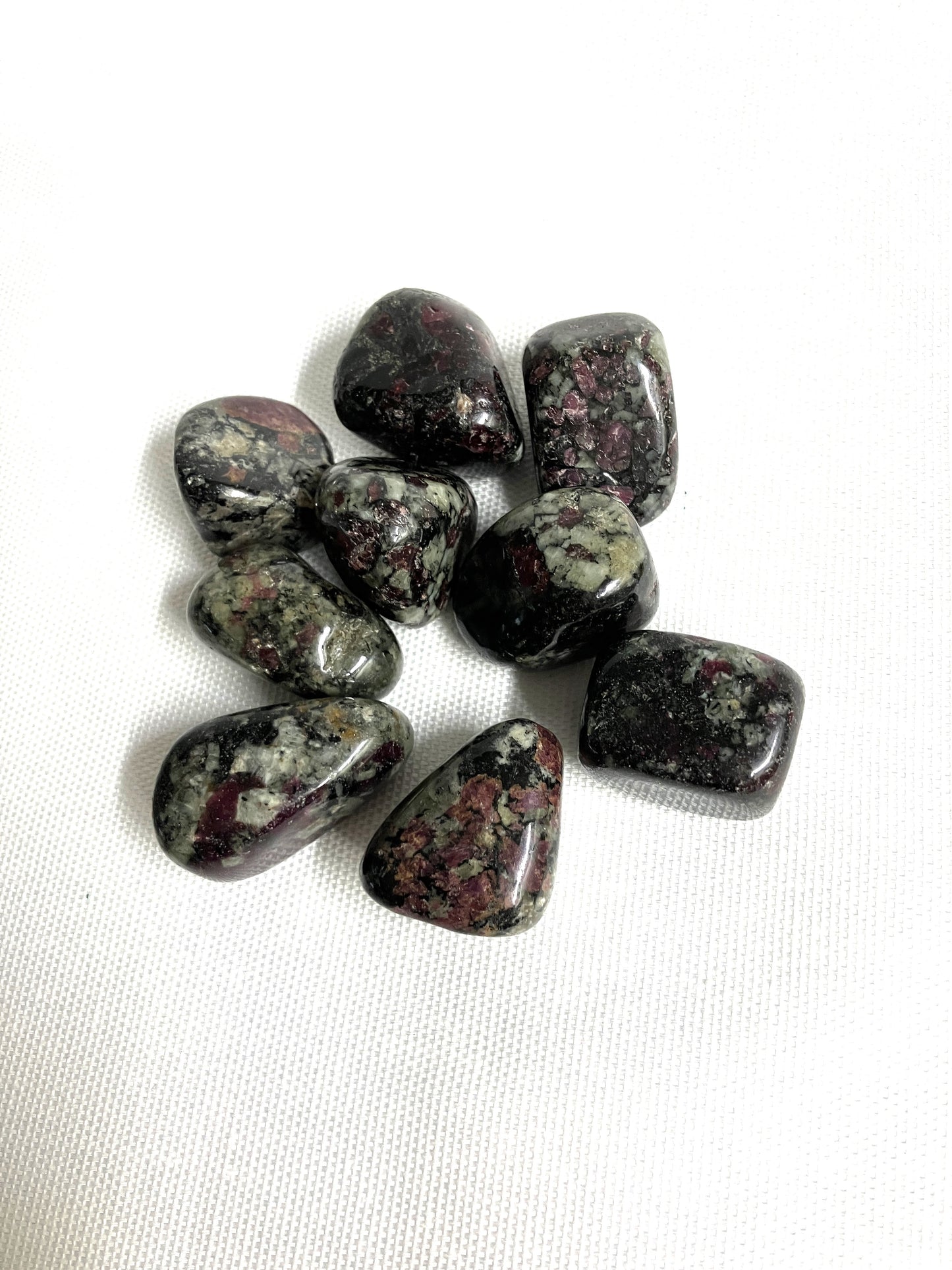 Collection of Eudialyte Tumbled Crystals showing the patterns and colors on a white background