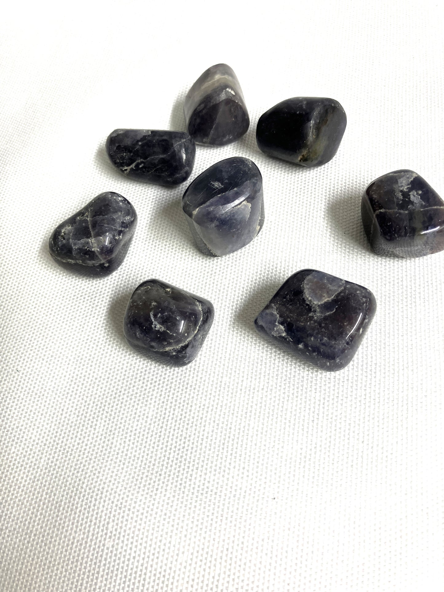 Tumbled Iolite Crystals arranged in a grid on a white fabric background