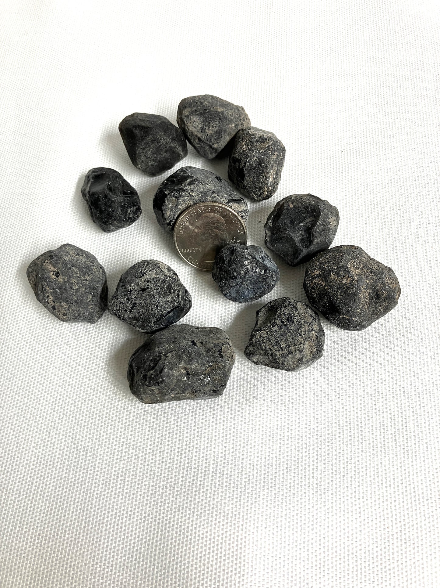 Rough Apache Tears with a quarter for scale on a white fabric background