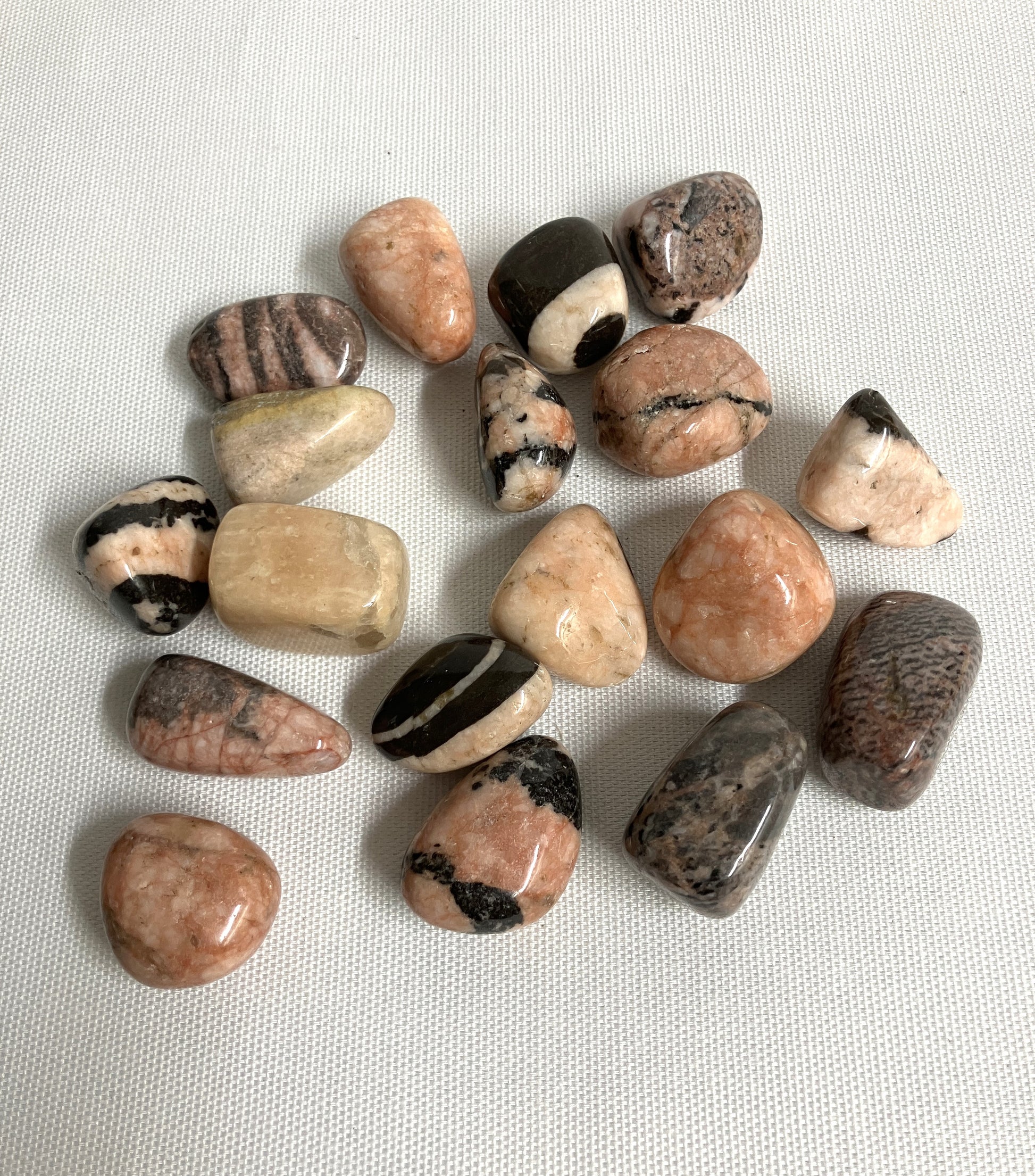 Group of Pink Zebra Jasper Crystals, variously shaped and colored placed on a light fabric background