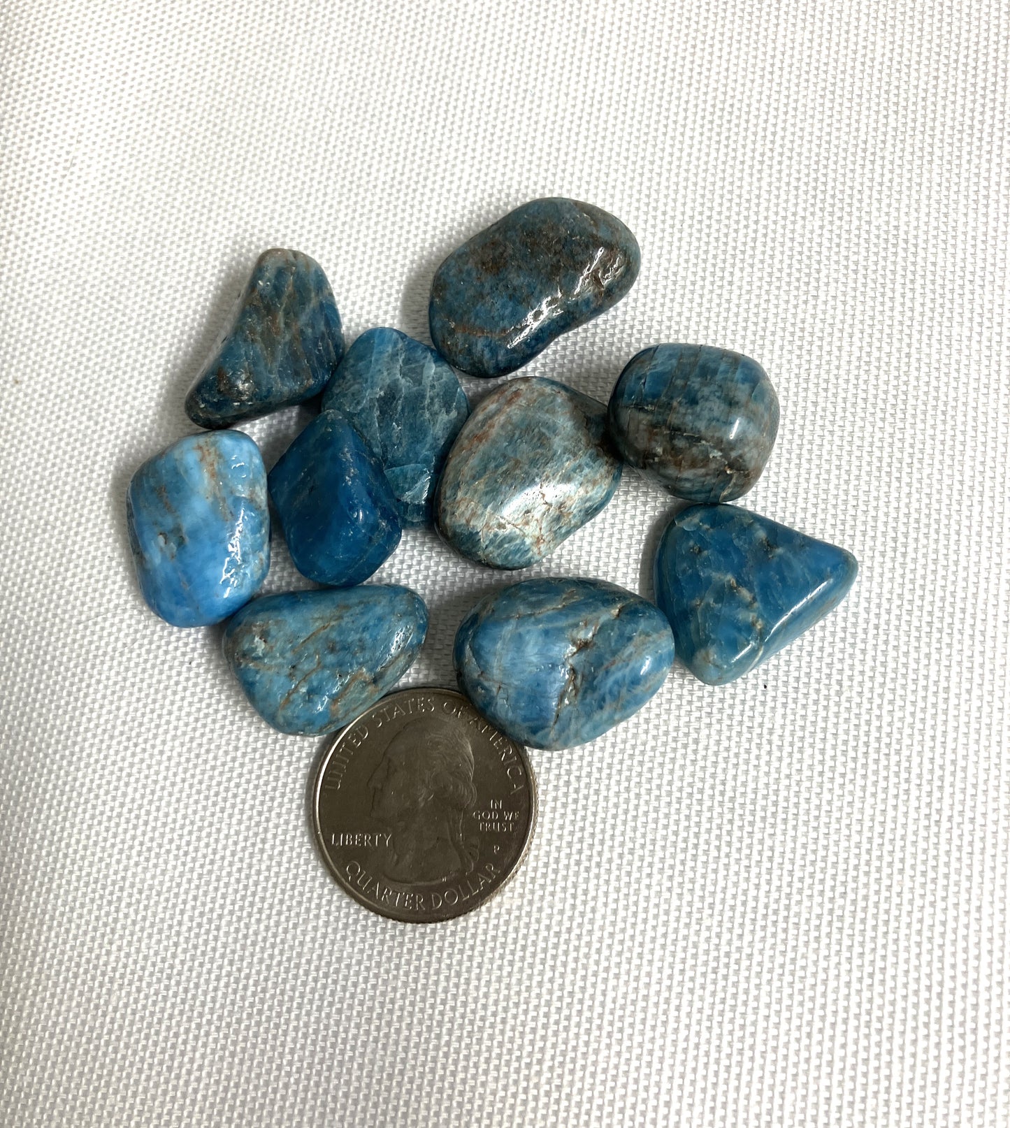Blue Apatite Crystals on a white background with a coin for scale
