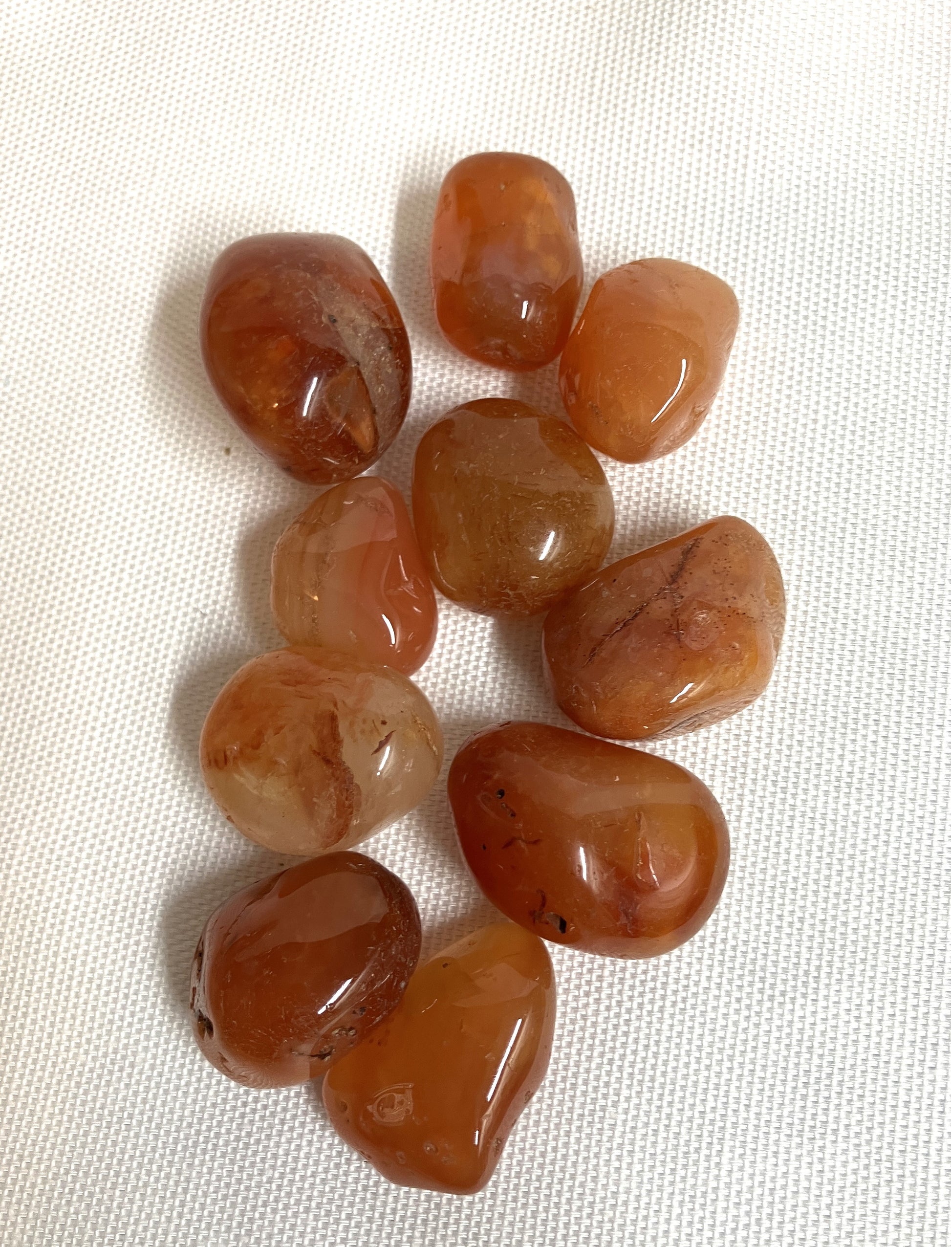 Collection of tumbled Carnelian Crystals on a white fabric background