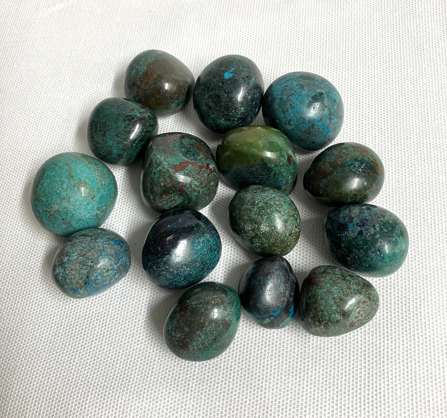 Tumbled Chrysocolla Crystals showing the variations of pattern and color on a white fabric background