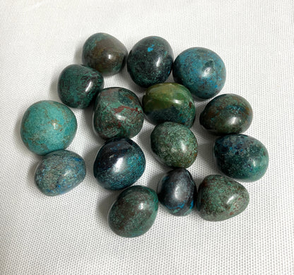 Tumbled Chrysocolla Crystals showing the variations of pattern and color on a white fabric background