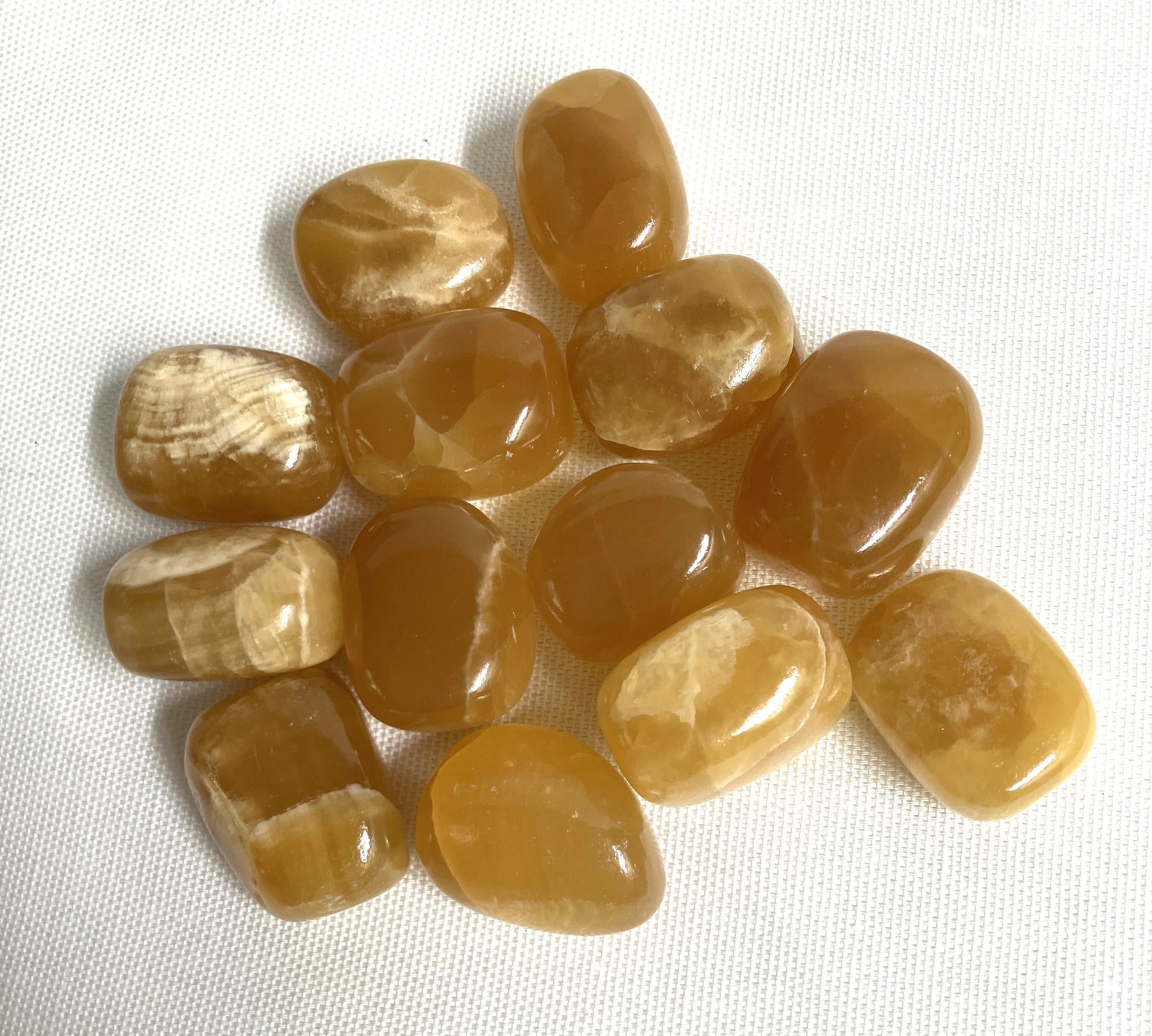 Tumbled Honey Caramel Calcite Crystals on a white fabric background