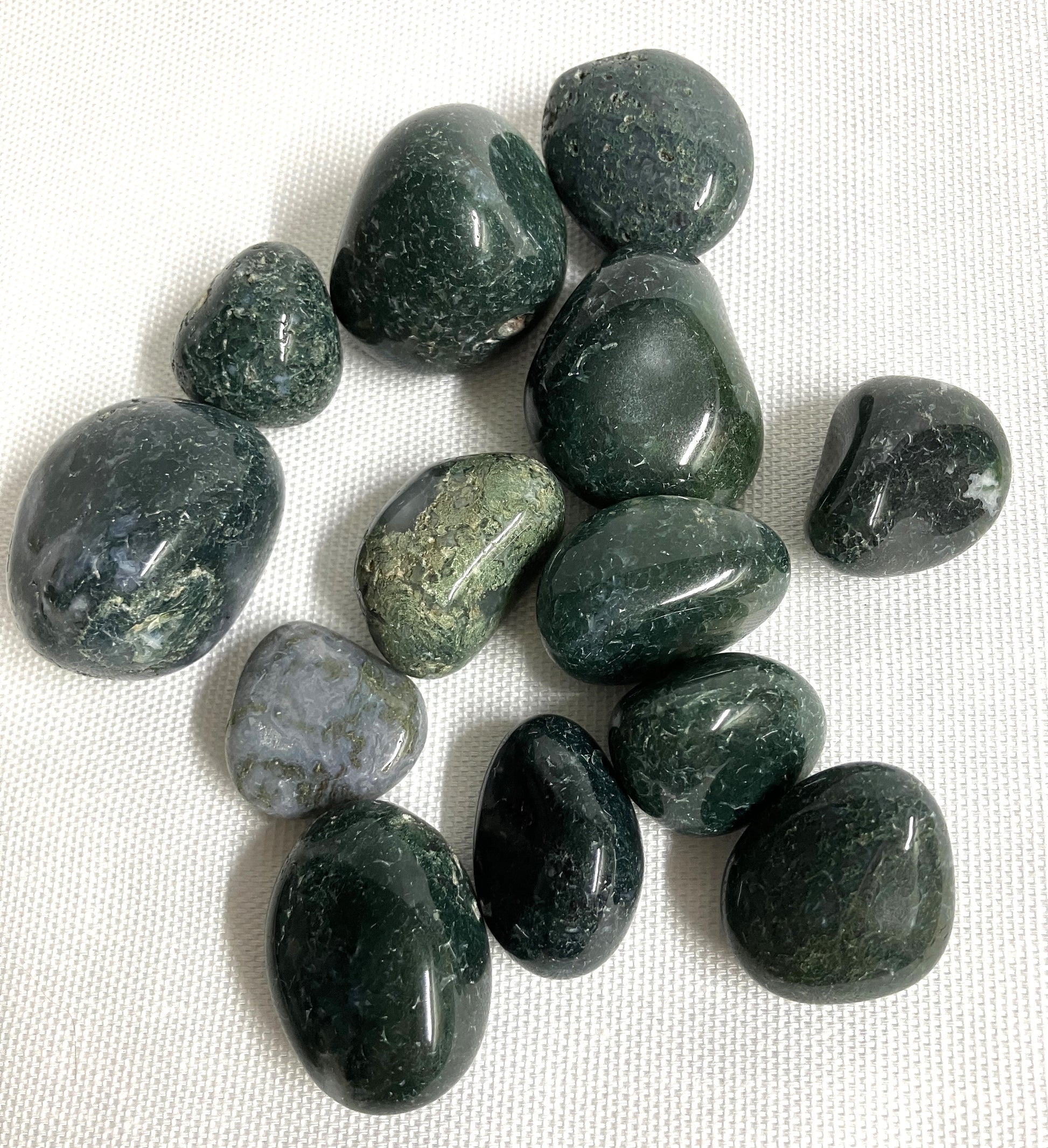 Collection of Moss Agate Crystals showing the back view on a white fabric background