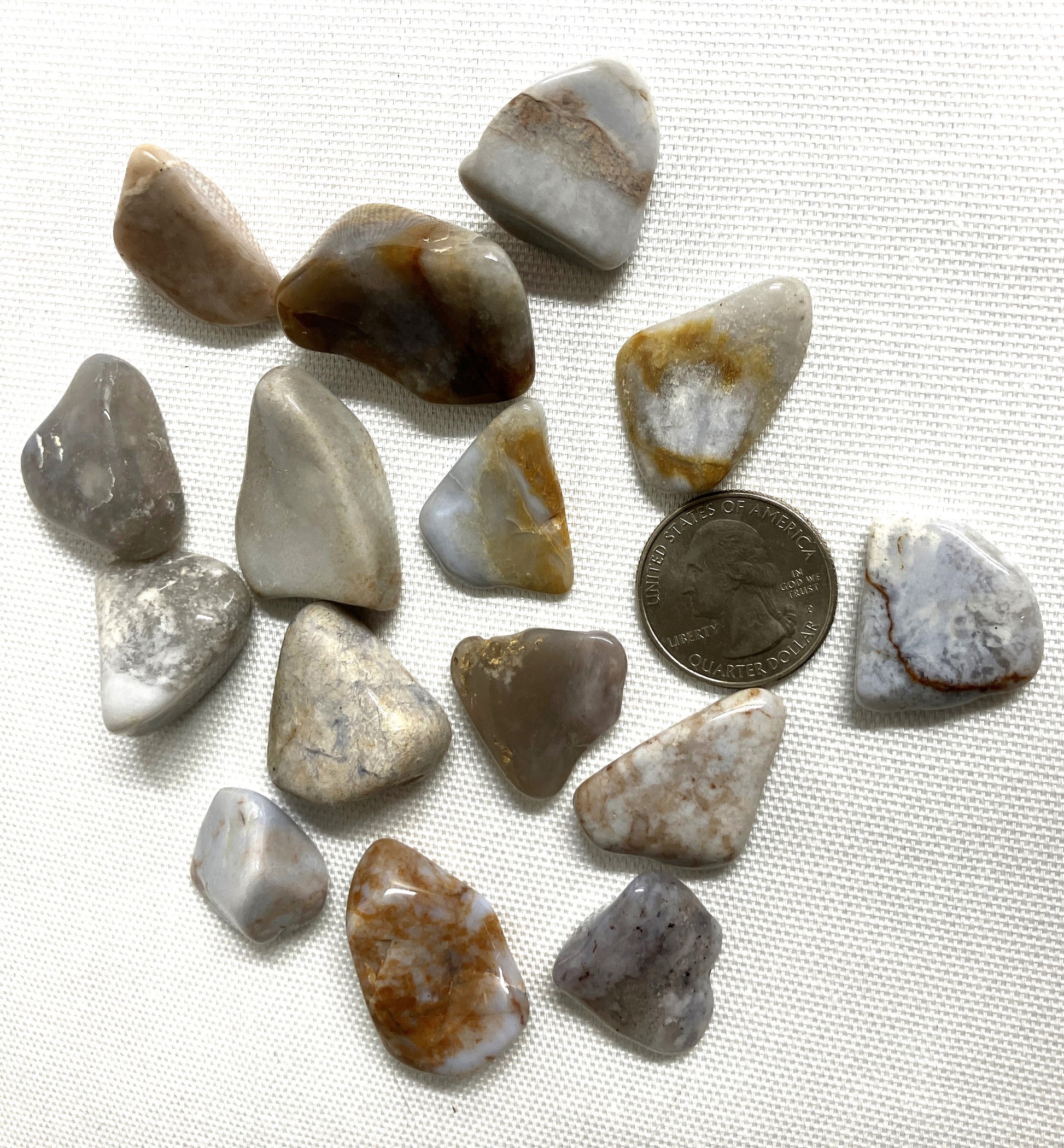 Collection of Blue Chalcedony Crystals on a white fabric background with a coin for scale.