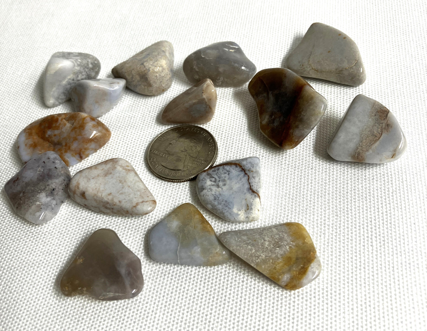 A second view of Blue Chalcedony Crystals with a coin for scale on a textured white surface