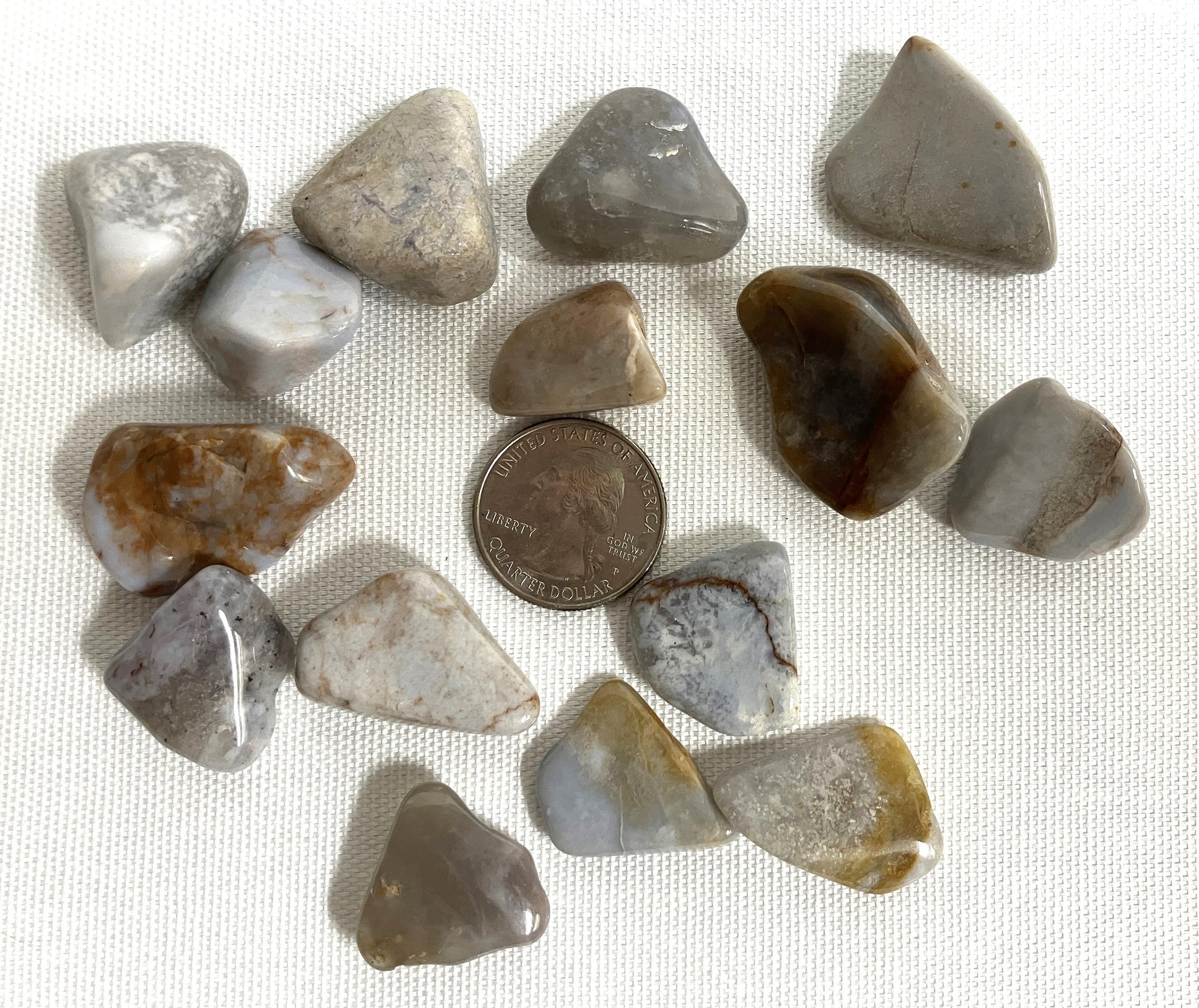 Blue Chalcedony Crystals shown with a quarter for scale on a white fabric background with a penny for scale.