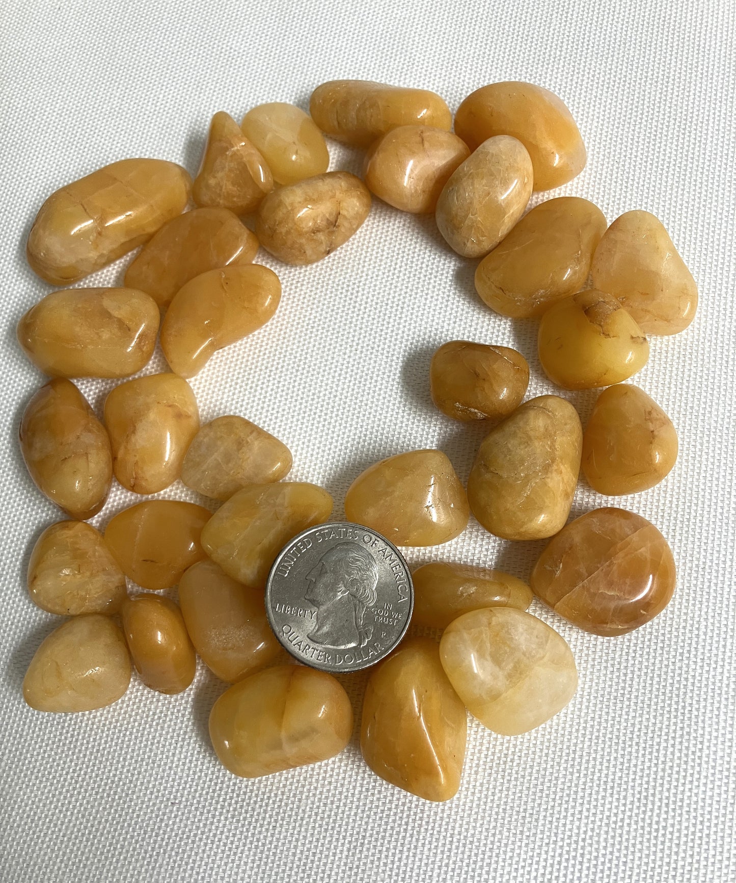 Round arrangement of Apricot Quartz Crystals with a quarter for scale on a white fabric background