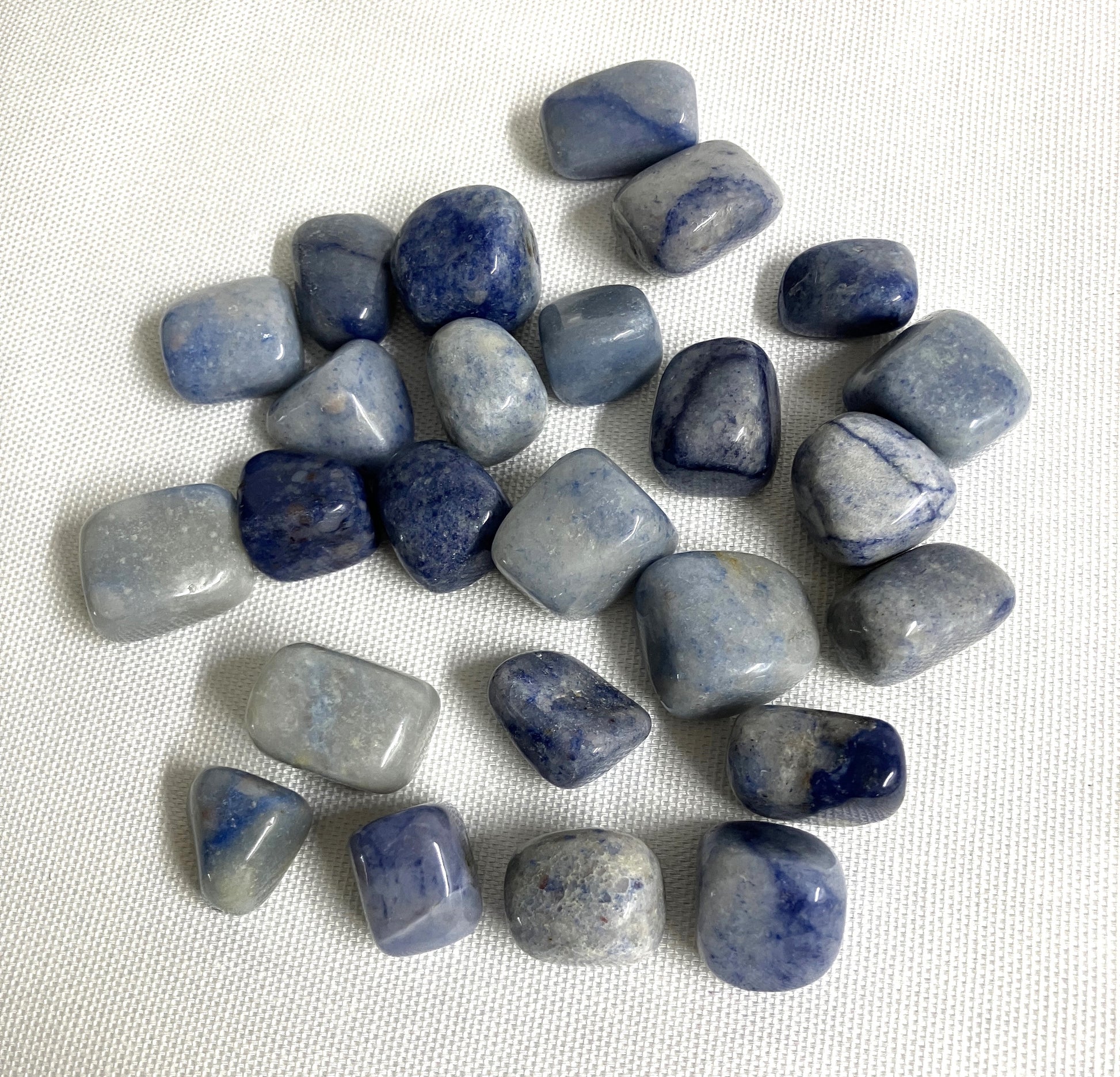 Collection of Tumbled Dumortierite Crystals showing a back side of a group of the crystals a white fabric background