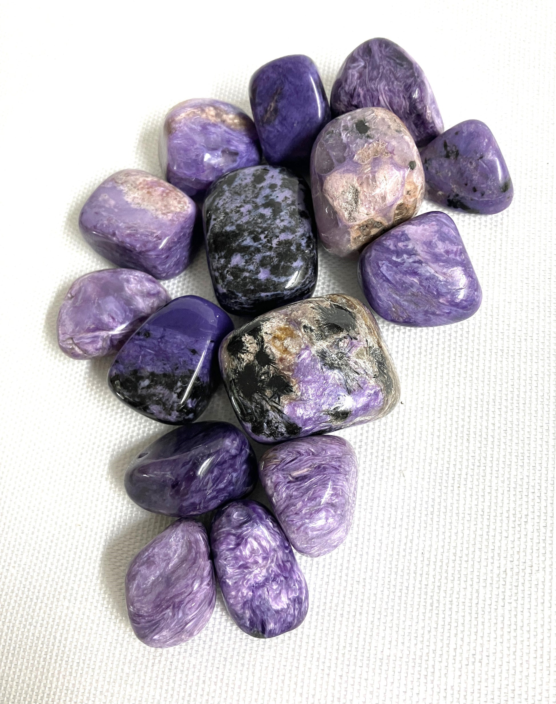 Close grouping of Charoite Tumbled Crystals on a white fabric background
