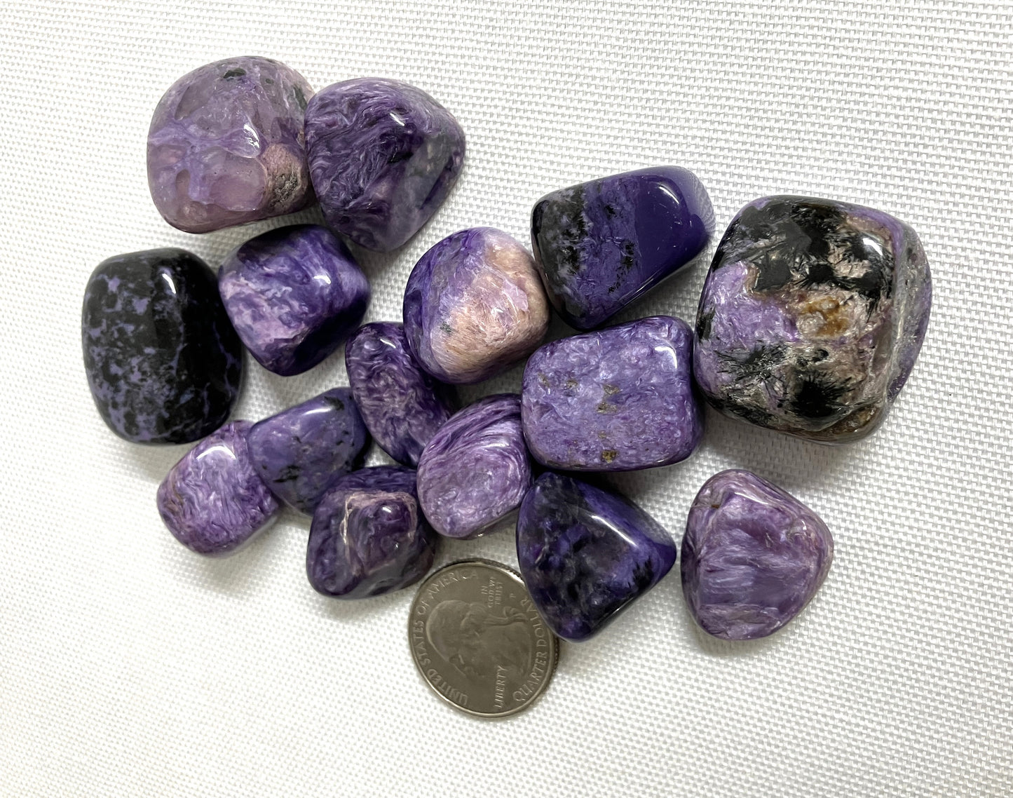 Closeup of Charoite Tumbled Crystals with a quarter for scale on a white background