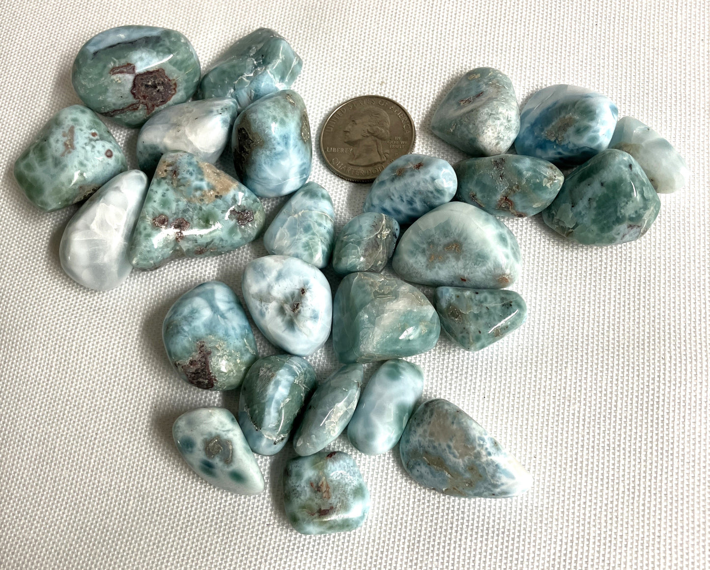 Another view of Larimar Crystals on a white fabric background with a coin for scale