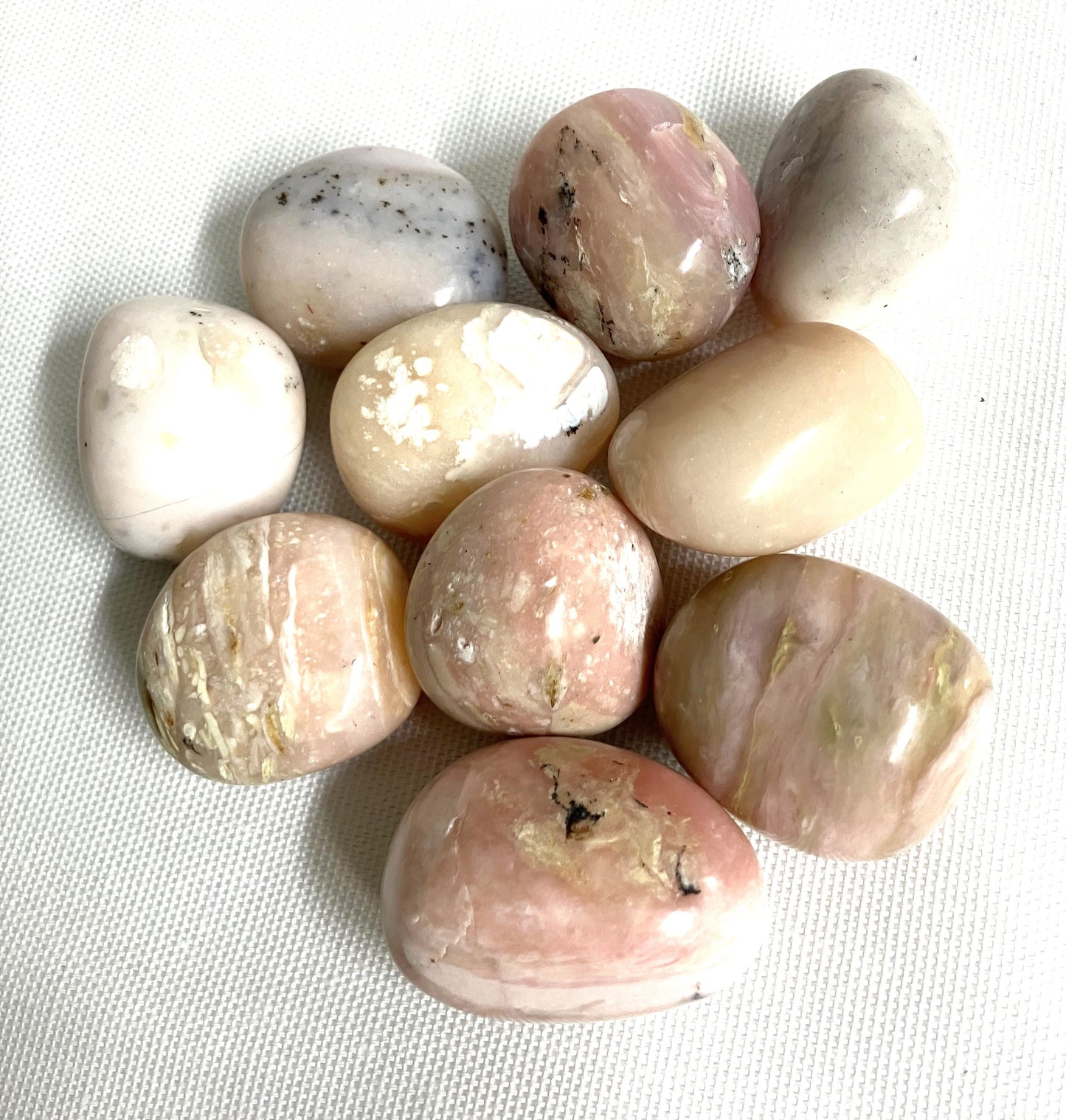 Collection of polished Pink Opal Crystals on a textured white surface