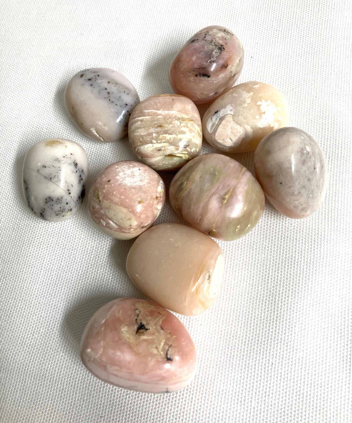 Collection of Pink Opal Crystals showing difference colors and patterns on a textured white surface