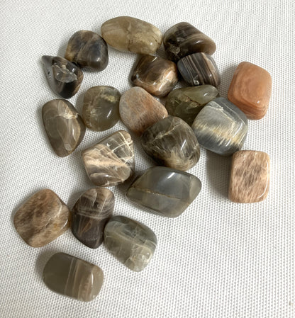 Tumbles Black Moonstone Crystals showing assorted patterns and colors on a light fabric background