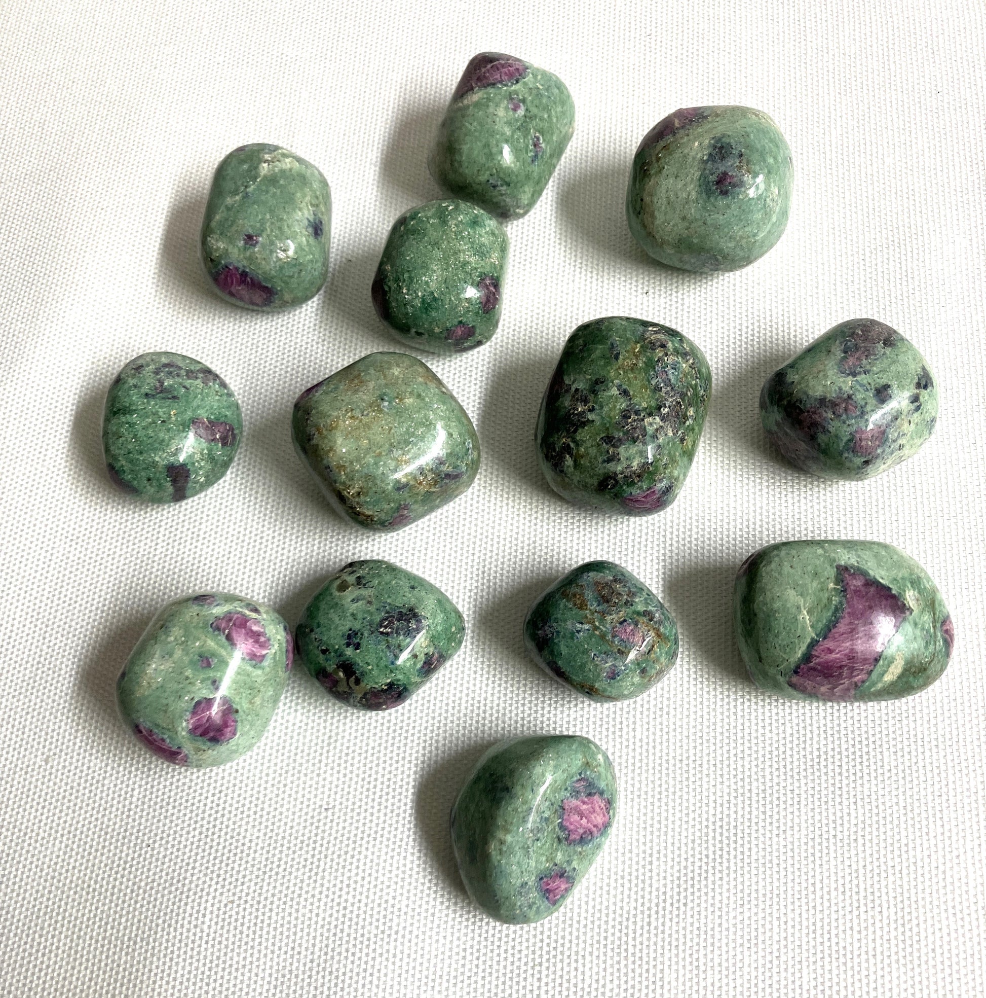Assorted Ruby Fuchsite Crystals showing the variation of patterns and colors on a white fabric background