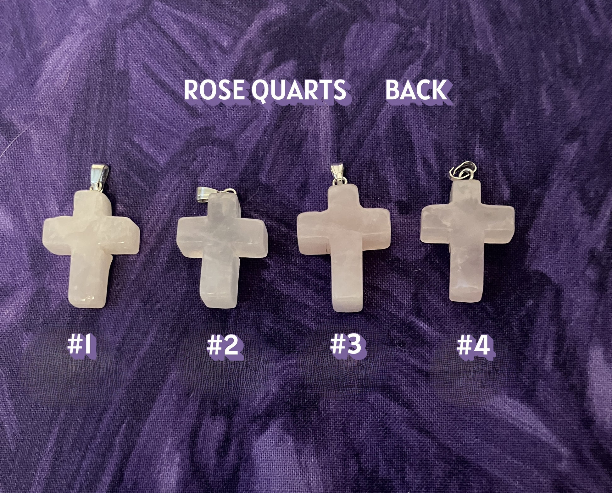 Back view of four cross-shaped rose quartz pendants on a purple textured background